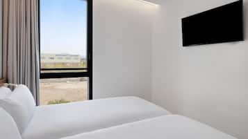 A hotel room with a large window, a bed, and a flat-screen TV mounted on the wall.