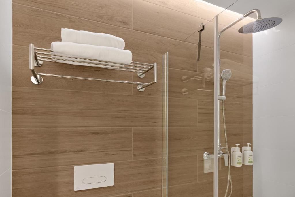 A shower with a handheld showerhead, a glass-enclosed shower stall, and a towel rack with two white towels.