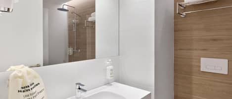 A modern bathroom with a white sink, mirror, and shower. There is a towel rack and a bag with text on it.