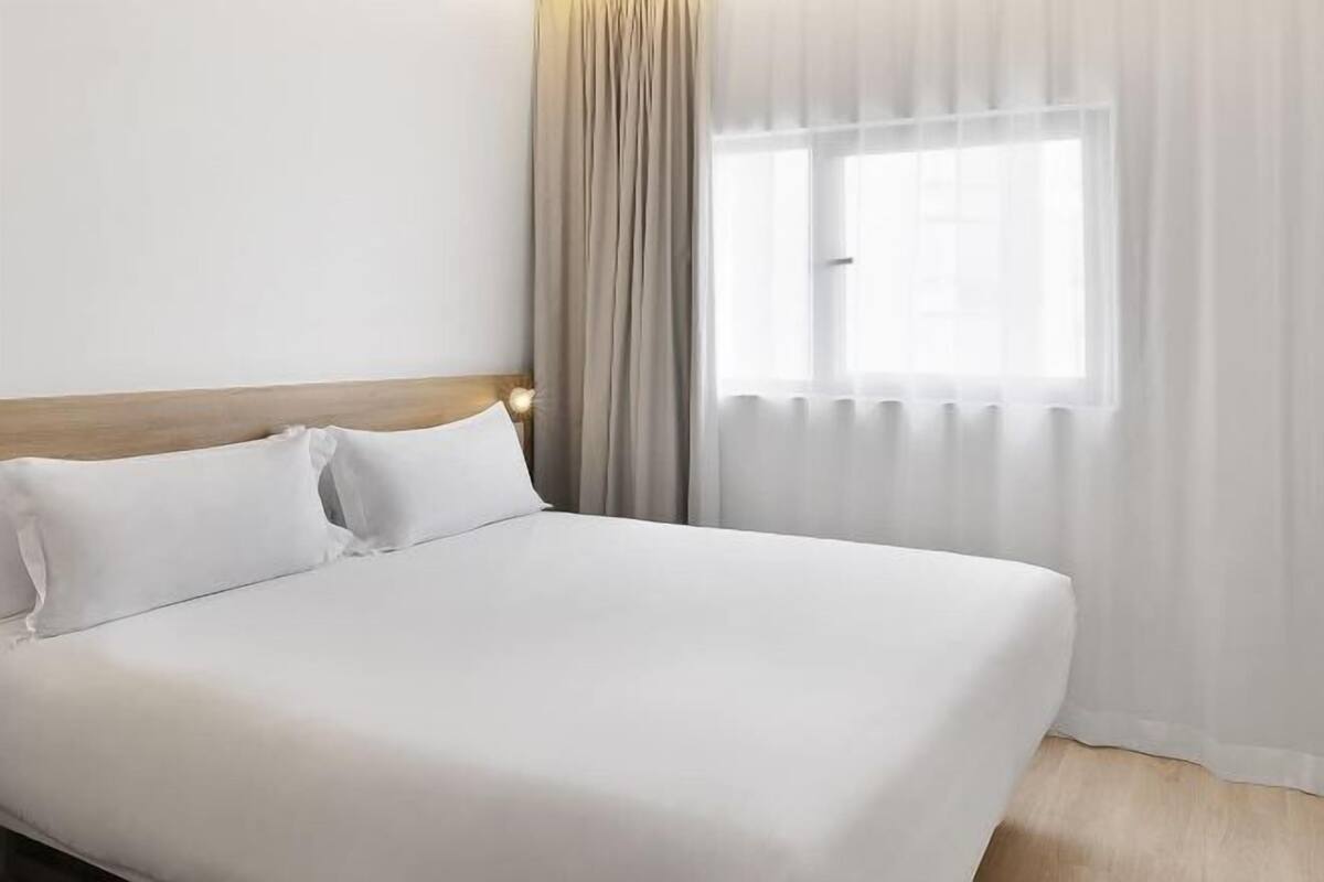 Et hotelværelse med seng, gardiner og et vindue.