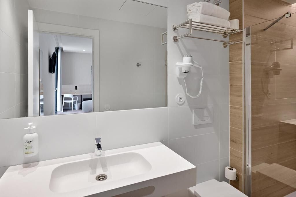 Un baño moderno con un lavamanos blanco, un espejo, una cabina de ducha de vidrio y un perchero para toallas.