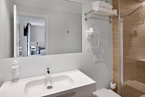 Et moderne badeværelse med hvid vask, spejl, brusekabine i glas og et håndklædestativ.