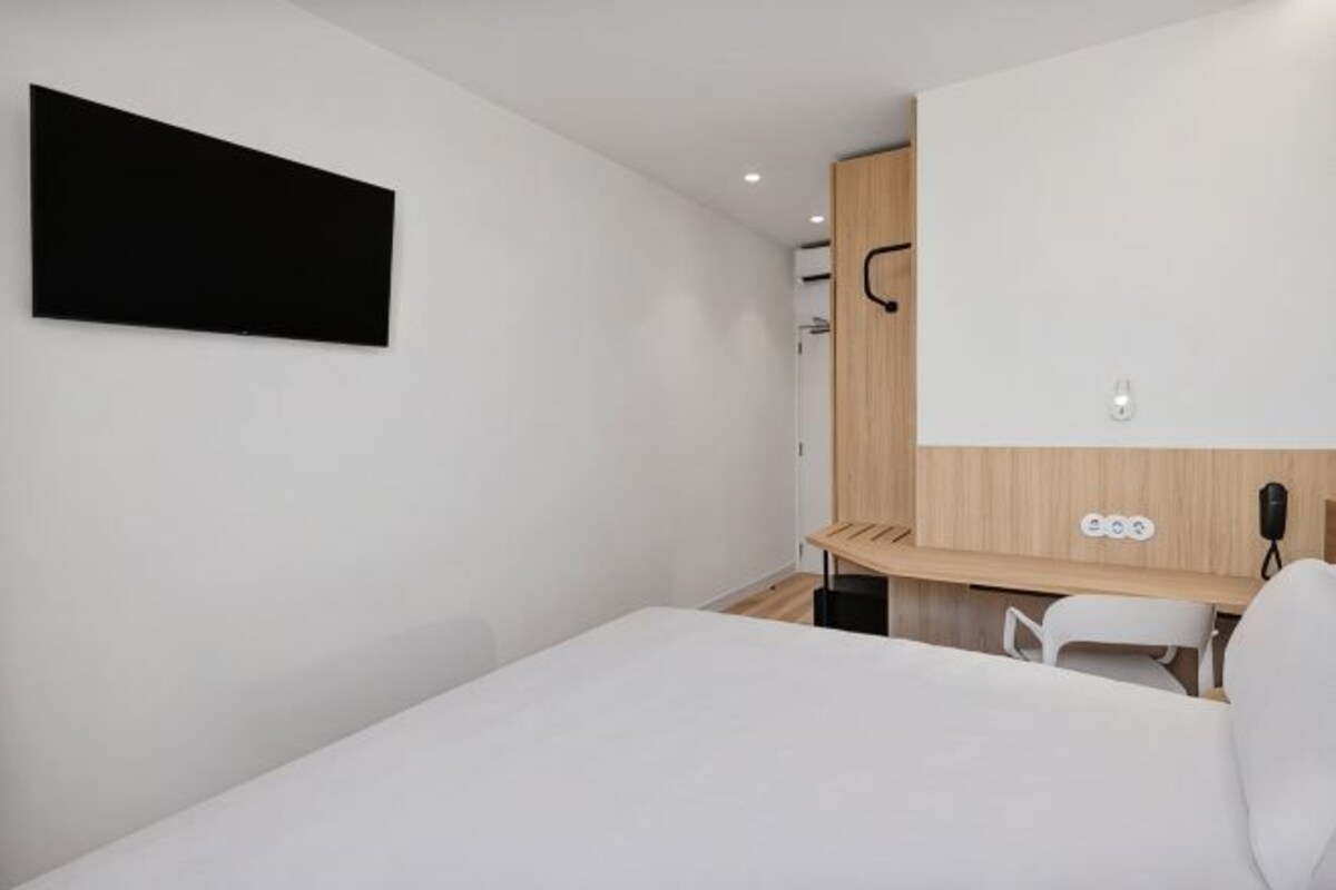 Une chambre d’hôtel moderne équipée d’un lit, d’un bureau, d’une chaise, d’un téléviseur à écran plat et d’un mur revêtu de panneaux en bois.