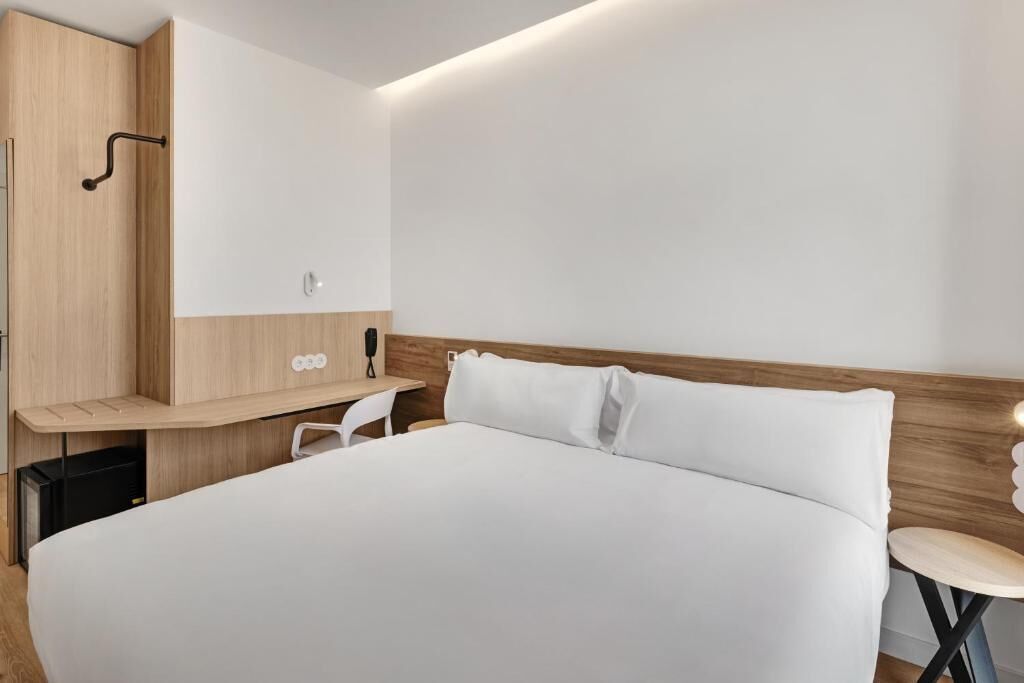 Una habitación de hotel moderna con una cama grande, un cabecero de madera, un escritorio pequeño y una silla.
