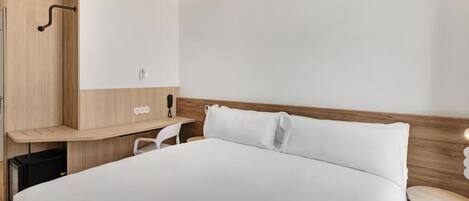 Una habitación de hotel moderna con una cama grande, un cabecero de madera, un escritorio pequeño y una silla.