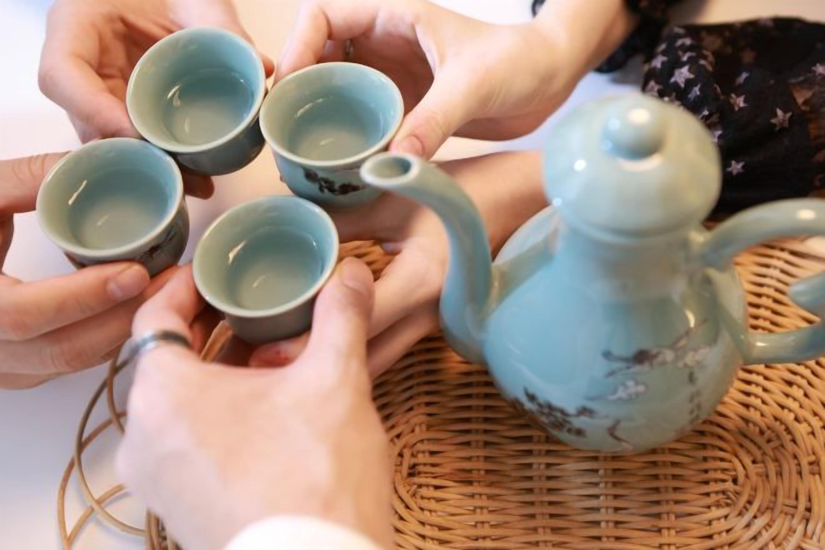 Un grupo de manos sosteniendo tazas, con una tetera sobre un tapete tejido.