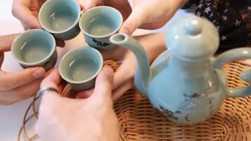 Un grupo de manos sosteniendo tazas, con una tetera sobre un tapete tejido.