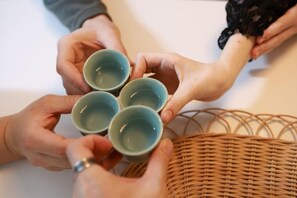 Des mains tenant quatre tasses, probablement pour une cérémonie du thé, avec un panier en osier en arrière-plan.