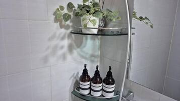 Baño con repisa de vidrio que sostiene una planta en maceta y tres botellas.