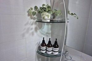 Une salle de bain avec une étagère en verre sur laquelle sont posés un pot de fleurs et trois bouteilles.