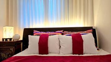 Una cama con ropa de cama blanca y roja, un cabecero de madera y una mesita de noche con una lámpara y un florero.