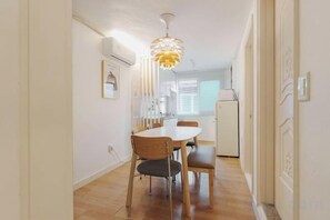 Un couloir étroit qui mène à un coin repas, avec une table ronde et des chaises, un luminaire au plafond et un réfrigérateur à l’arrière-plan.