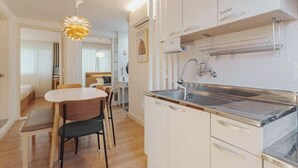 Cocina compacta con armarios blancos, un lavamanos de acero inoxidable y una lámpara colgante.