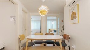 Un comedor con una mesa y sillas blancas, un banco y un accesorio de luz decorativo.