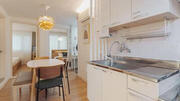 Cocina compacta con encimera blanca, un lavamanos y armarios. Cuenta con una zona de comedor con mesa y sillas.