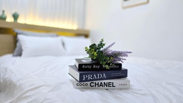Una cama bien hecha con una pila de libros y una planta pequeña encima.