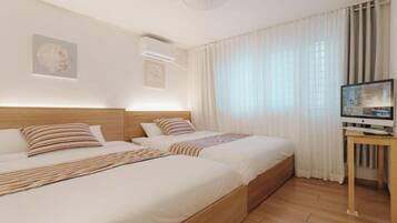 A hotel room with two beds, a television on a stand, and a window with curtains.