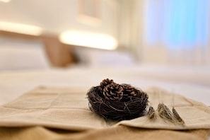 Una piña de pino y plumas dispuestas ordenadamente sobre un paño color beige en una habitación con fondo desenfocado.