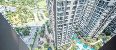 A high-rise building with multiple balconies overlooking a landscaped area with a swimming pool.