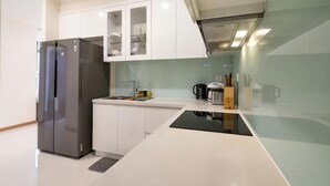 A modern kitchen with a built-in refrigerator, white cabinets, and a black countertop. - The Peninsula Apartment Landmark (Ho Chi Minh City)