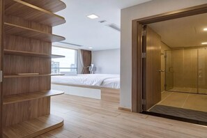 A modern hotel room with a built-in bed, a wooden shelving unit, a shower area, and a view of the city. - The Peninsula Apartment Landmark (Ho Chi Minh City)
