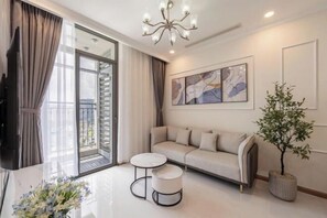 Una sala de estar moderna con un sofá, dos mesas auxiliares, un televisor y un ventanal con cortinas.