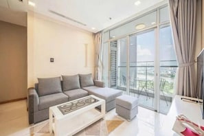 A modern living room with a grey sofa, a white coffee table, and a balcony with a glass door. - The Peninsula Apartment Landmark (Ho Chi Minh City)
