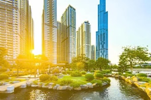 Un paisaje urbano moderno con rascacielos, una fuente de agua y abundante vegetación.