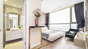 A modern hotel room with a large bed, a sitting area with a chair, a desk, and a large window offering a city view. - The Peninsula Apartment Landmark (Ho Chi Minh City)