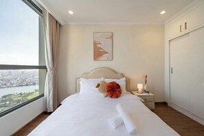 A hotel room with a large window, a bed with white linens, a nightstand with a lamp, and a painting on the wall. - The Peninsula Apartment Landmark (Ho Chi Minh City)