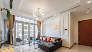 A modern living room with a sofa, a glass coffee table, a floor lamp, and a view through large glass doors. - The Peninsula Apartment Landmark (Ho Chi Minh City)
