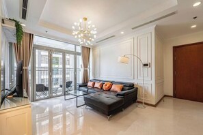 A modern living room with a sofa, a glass coffee table, a floor lamp, and a view through large glass doors. - The Peninsula Apartment Landmark (Ho Chi Minh City)