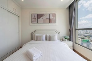 A hotel room with a large bed, a nightstand, a window with a city view, and a framed artwork on the wall. - The Peninsula Apartment Landmark (Ho Chi Minh City)