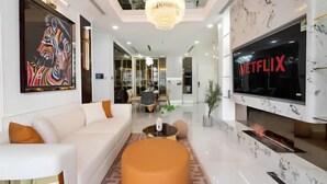 A modern living room with a white sofa, a large TV screen, and a chandelier. - The Peninsula Apartment Landmark (Ho Chi Minh City)