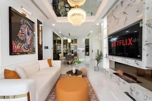 Una sala de estar moderna con un sofá blanco, una pantalla de televisión grande y una araña.