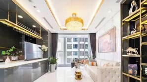 A modern living room with a chandelier, a sofa, a coffee table, and a bookshelf. - The Peninsula Apartment Landmark (Ho Chi Minh City)
