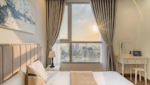 A bedroom with a bed, a vanity with a mirror, and a view of the city through a window. - The Peninsula Apartment Landmark (Ho Chi Minh City)