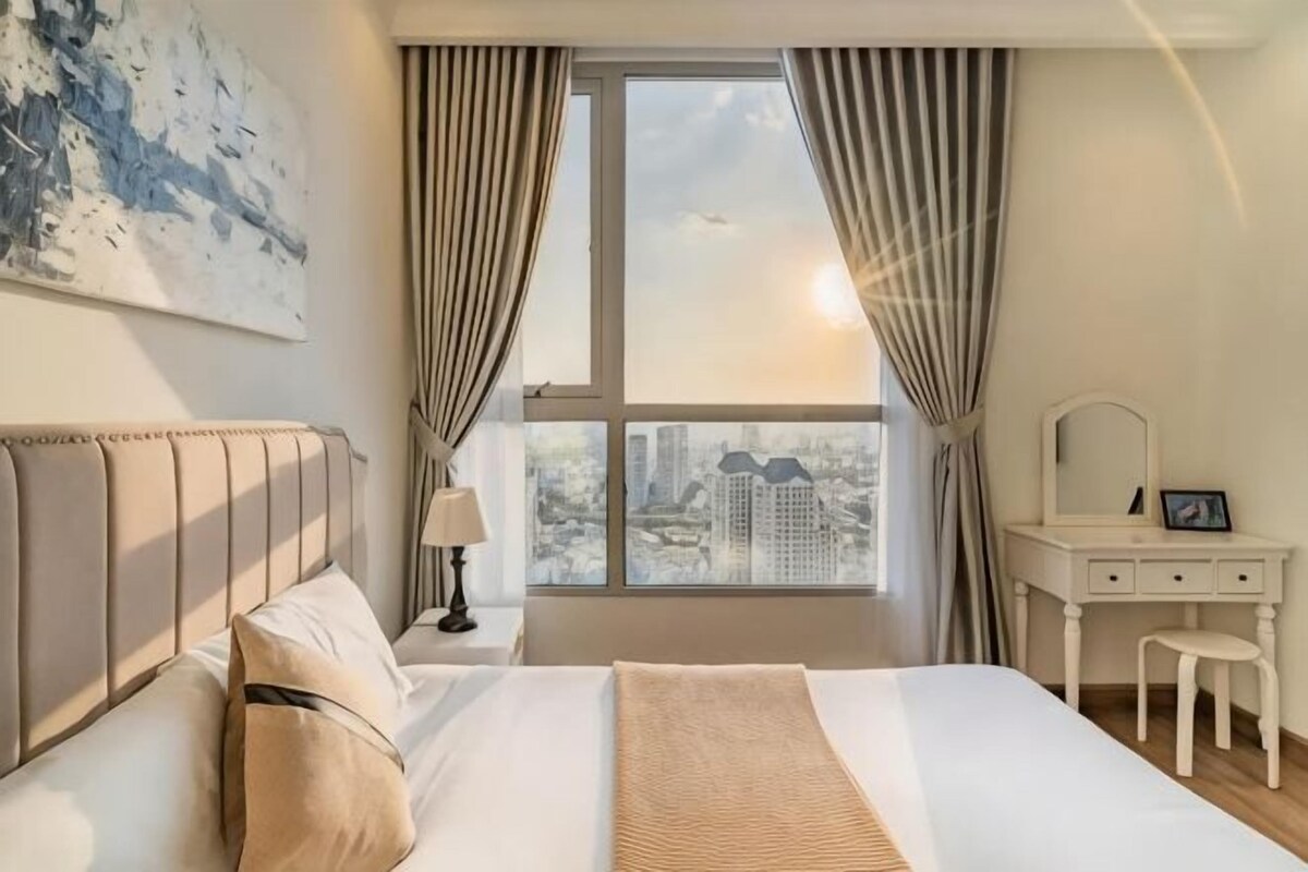 Un dormitorio con cama, tocador con espejo y vistas a la ciudad a través de una ventana.