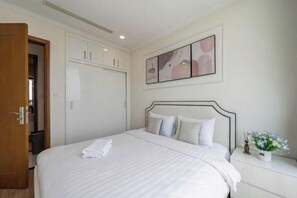 Una cama bien hecha con cabecera blanca, una mesita de noche con un jarrón de flores y una obra de arte abstracta colgada en la pared.