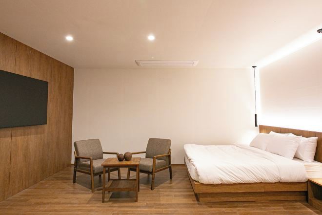 Un dormitorio moderno con suelo de madera, una cama grande con ropa blanca, dos sillones, una mesita y un televisor de pared.