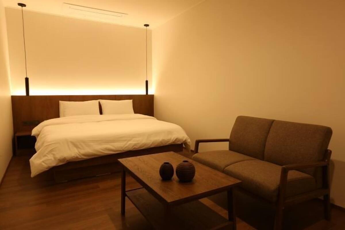 A bedroom with a bed, a sofa, a small table, and two vases.