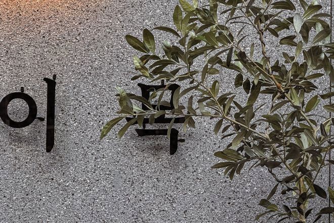 Una pared con un letrero negro grande y una planta de hojas verdes.