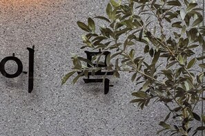 A wall with a large black sign and a plant with green leaves. - Hotel Emok (Busan)