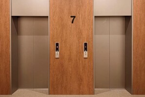 Un ascenseur doté d’une porte en bois portant le numéro 7 et muni de deux panneaux de commande.