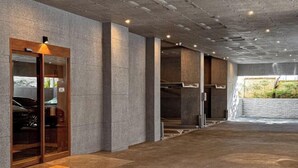 A modern hotel lobby with a concrete floor, large pillars, and a glass elevator entrance. - Hotel Emok (Busan)