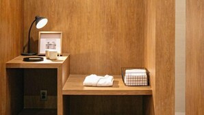 A wooden room with a desk, a lamp, a framed picture, a white mug, a folded towel, and a grid-patterned basket. - Hotel Emok (Busan)