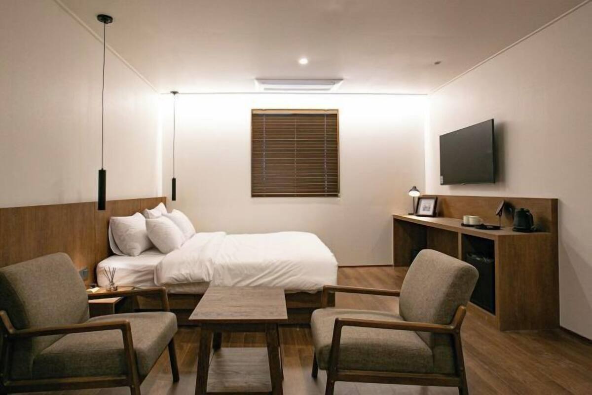 A bedroom with a bed, bedside tables, a desk, chairs, a TV, and a window with blinds.