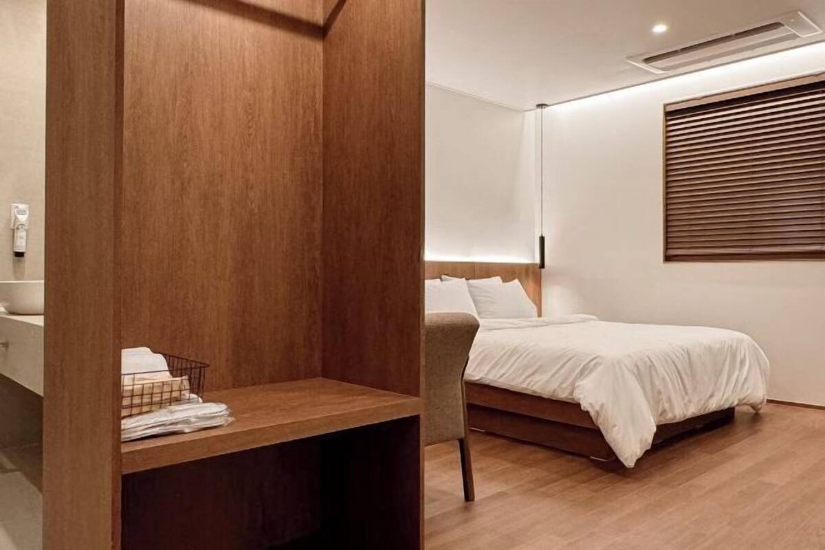 A modern bedroom with a wooden headboard, a bed with white bedding, a wooden nightstand, and a wall-mounted air conditioning unit.