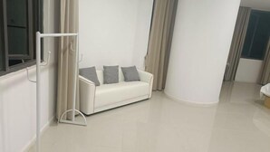 A modern, minimalist living room with a white sofa and grey cushions, a white floor lamp, and a window with curtains. - Five Tigers Hotel (Boten)