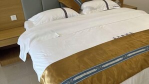 A neatly made bed with white and brown bedding, a wooden headboard, and a bedside table with a lamp. - Five Tigers Hotel (Boten)